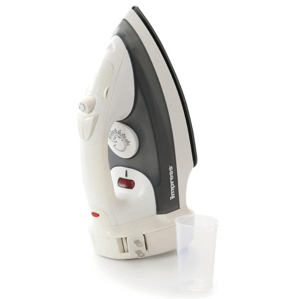White and black Impress steam iron standing upright with a temperature dial, steam control knob, and red indicator light—next to a small transparent measuring cup.