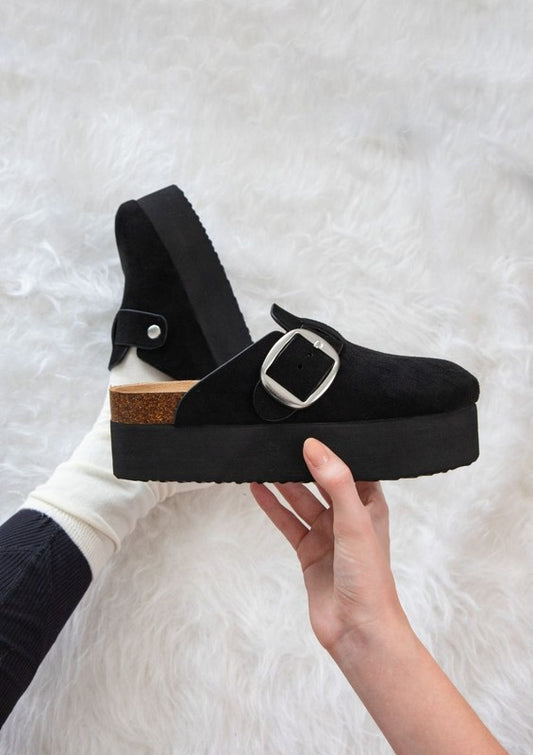 Chunky platform mules featuring adjustable ankle strap with buckle, closed-toe cut, layered flatform sole, slip-on design