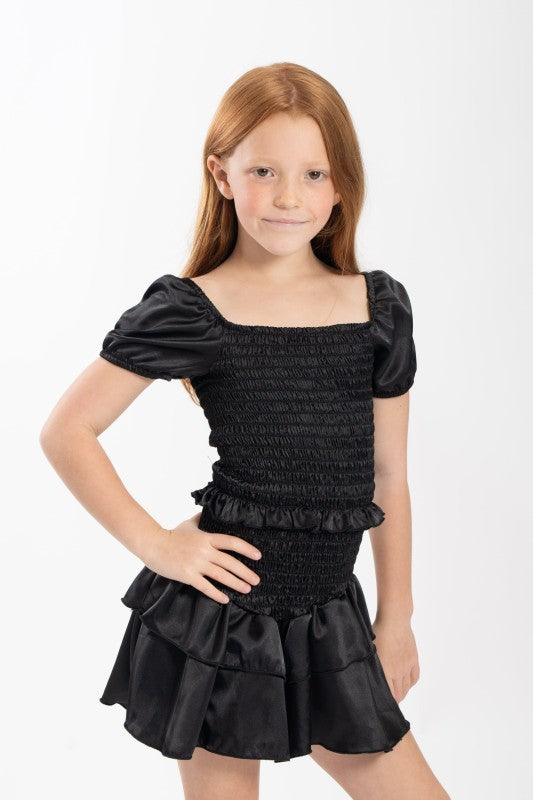 Young girl wearing a black smocked dress with puffed sleeves on a white background