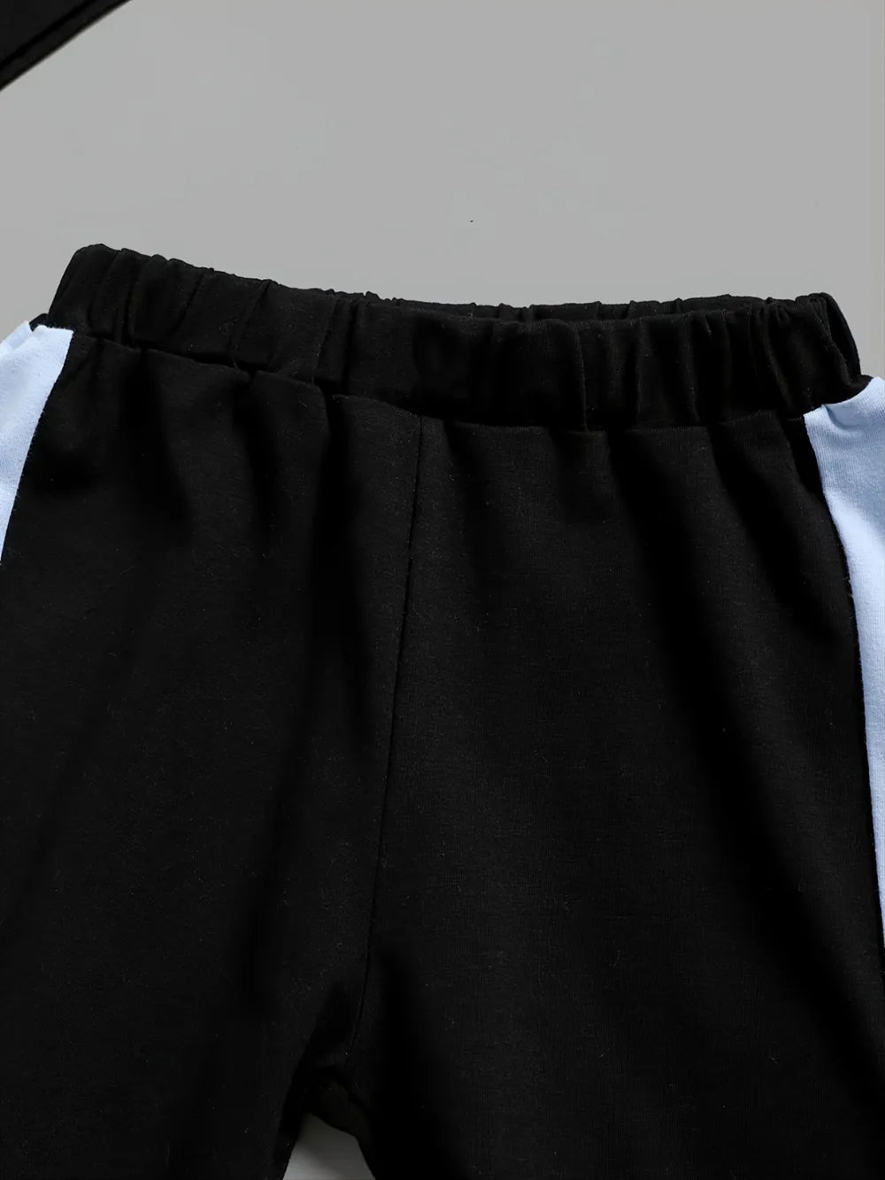 Black pants with a white shirt underneath on a light gray background