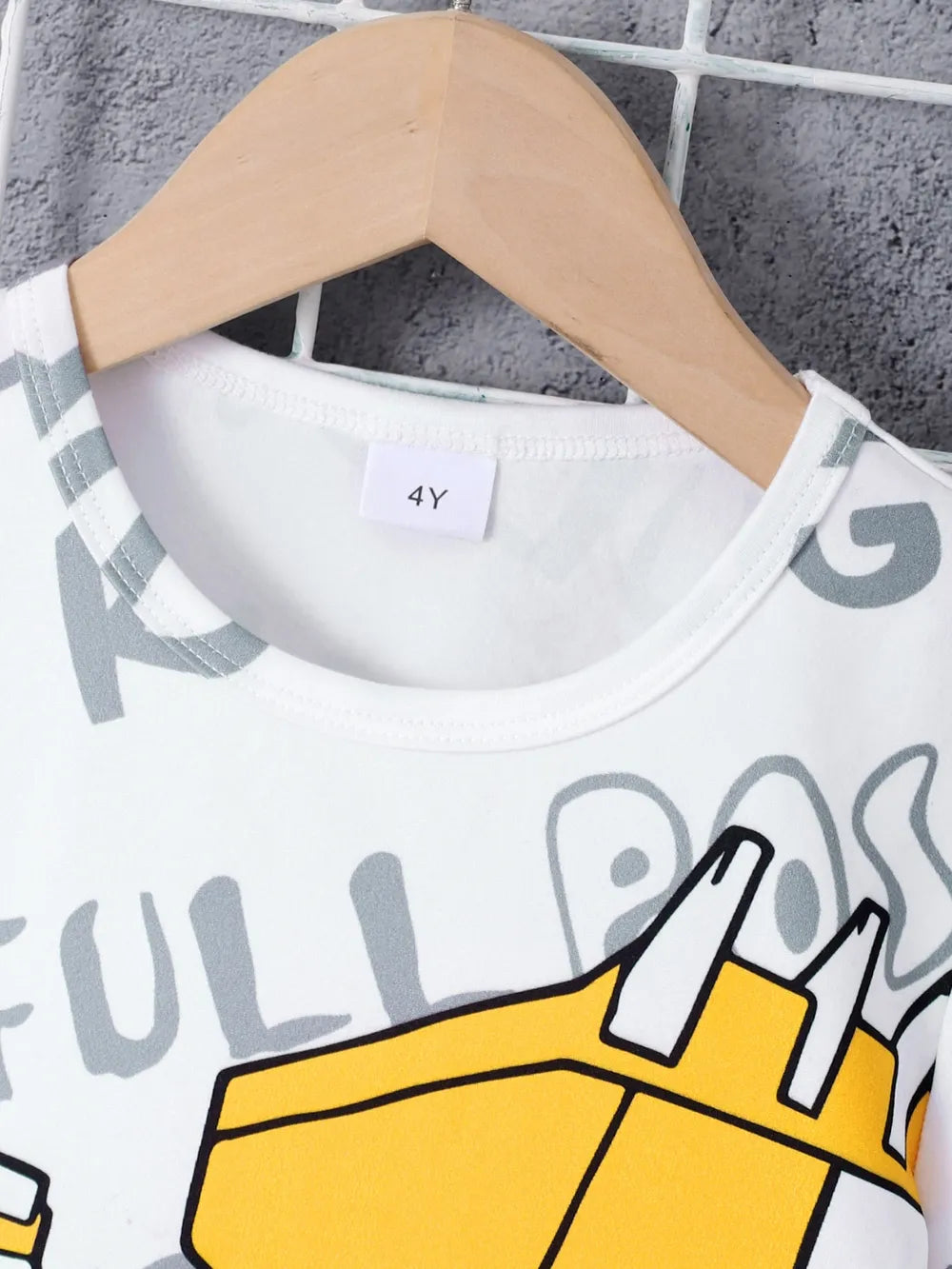 Children's t-shirt with cartoon design on a hanger against a textured wall.