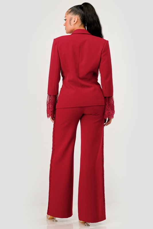 A woman in a red pantsuit. This bold suit features a deep V-neck blazer with lace accents on the sleeves and sides of the pants. 