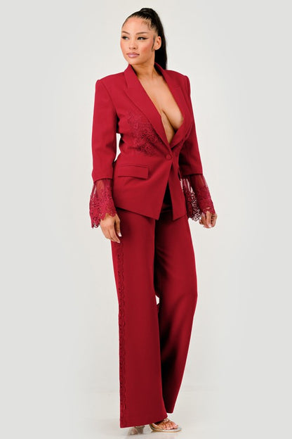 A woman in a red pantsuit. This bold suit features a deep V-neck blazer with lace accents on the sleeves and sides of the pants. 