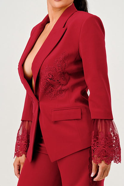 A woman in a red pantsuit. This bold suit features a deep V-neck blazer with lace accents on the sleeves and sides of the pants. 