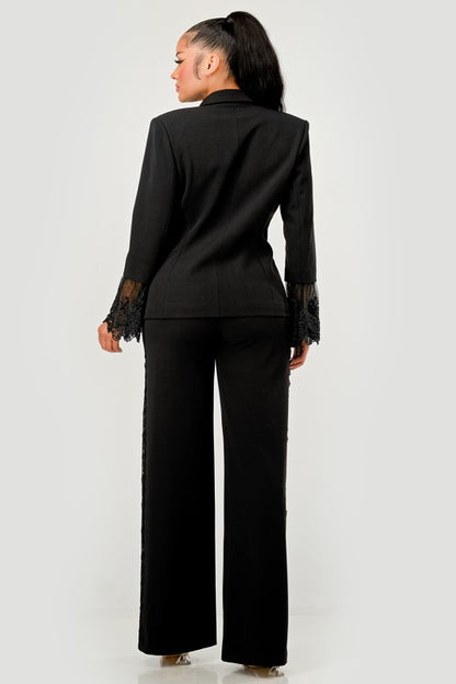 A woman in a black pantsuit. This bold suit features a deep V-neck blazer with lace accents on the sleeves and sides of the pants. 