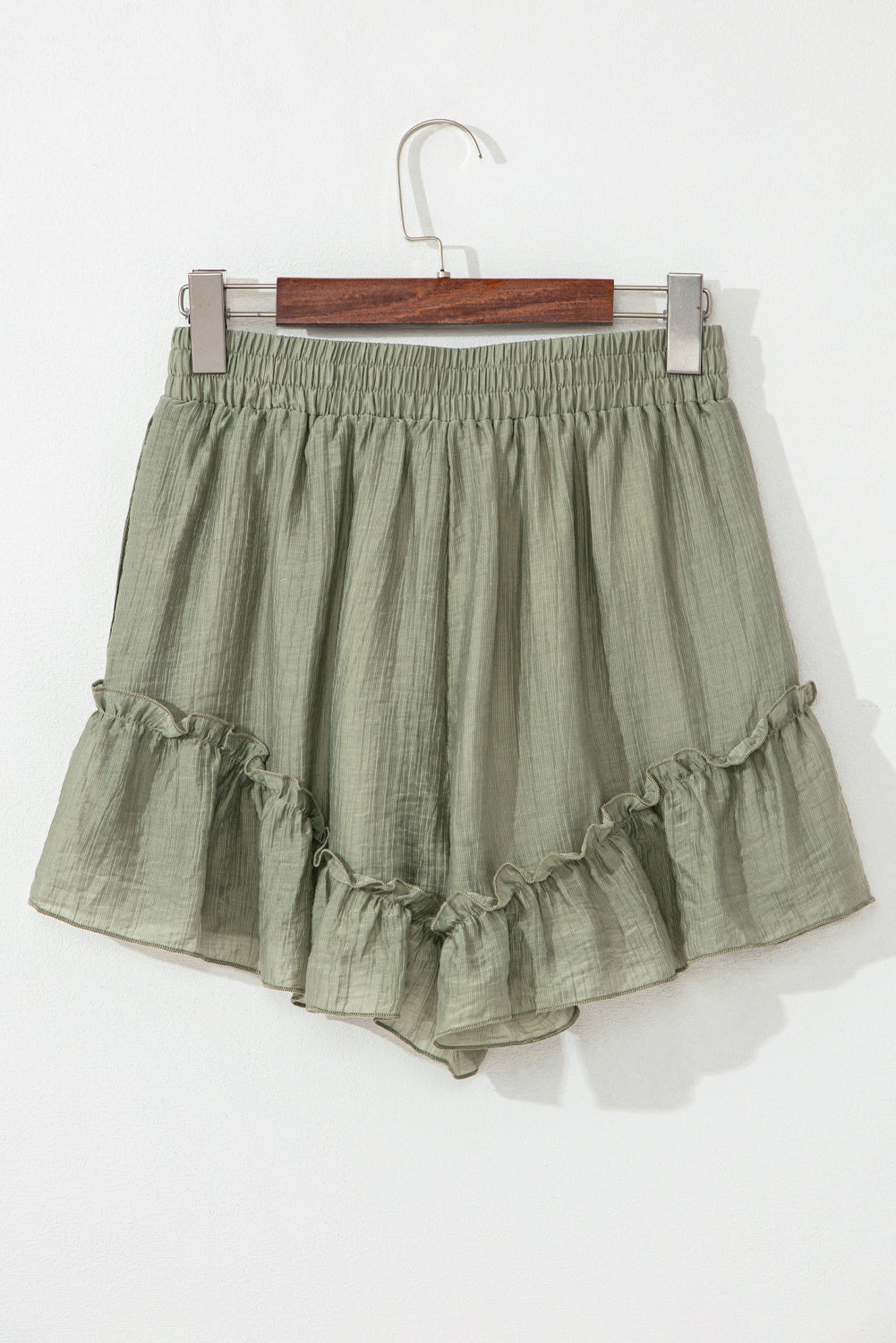 A close-up of light green, textured shorts with a drawstring waist and ruffled hem, displayed against a neutral background.
