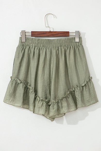 A close-up of light green, textured shorts with a drawstring waist and ruffled hem, displayed against a neutral background.