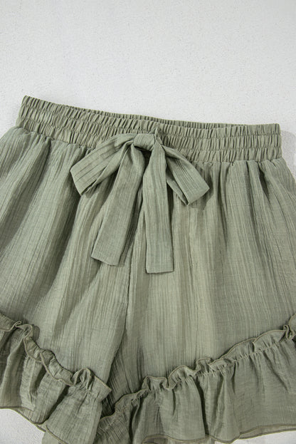 A close-up of light green, textured shorts with a drawstring waist and ruffled hem, displayed against a neutral background.