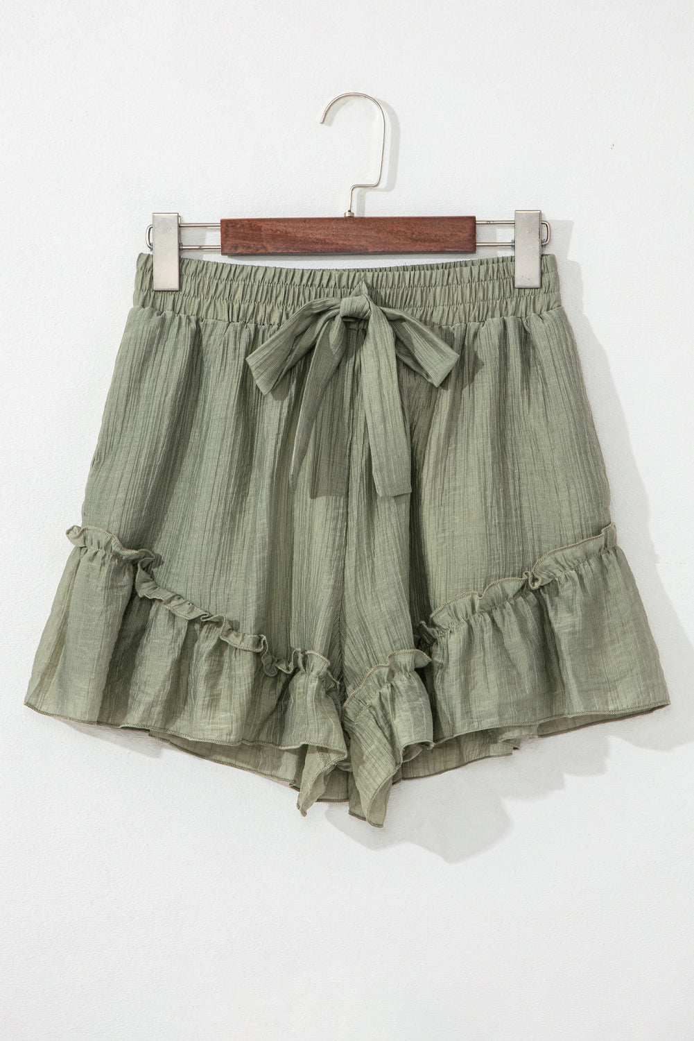 A close-up of light green, textured shorts with a drawstring waist and ruffled hem, displayed against a neutral background.