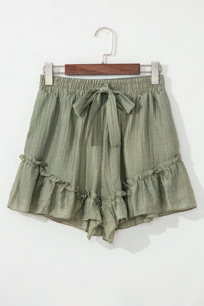 A close-up of light green, textured shorts with a drawstring waist and ruffled hem, displayed against a neutral background.