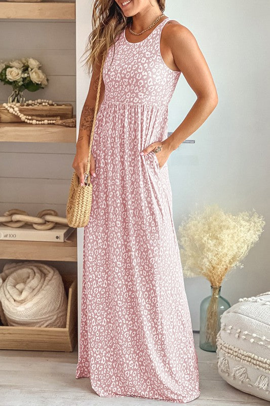 A woman in a pink sleeveless maxi dress with a leopard print, posing in a cozy room.
