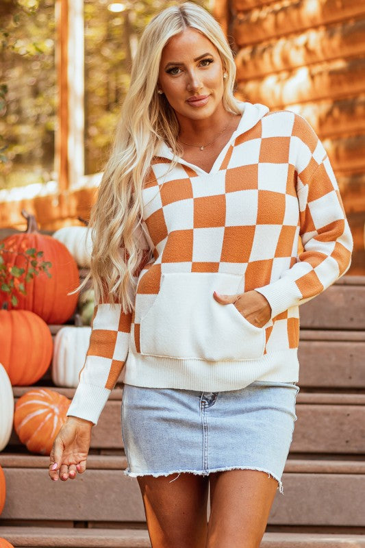 Woman wears a cozy orange and white checkered hooded sweater with a kangaroo pocket.