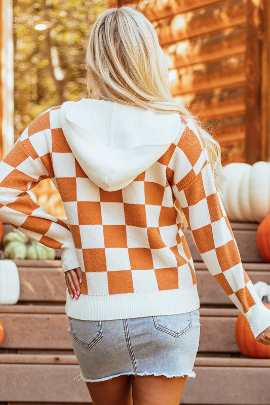 Woman models a cozy orange and white checkered hooded sweater with a kangaroo pocket.