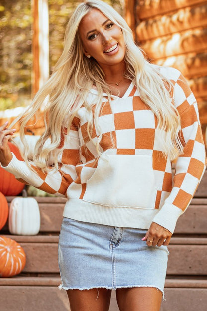 Woman wears a cozy orange and white checkered hooded sweater with a kangaroo pocket, with fingers running through hair.