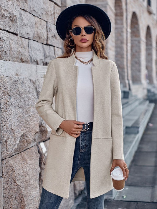 A lady rocking a chic outfit - a long beige coat over a white top, paired with blue jeans. She's accessorizing with a black hat, sunglasses, and some cool jewelry.