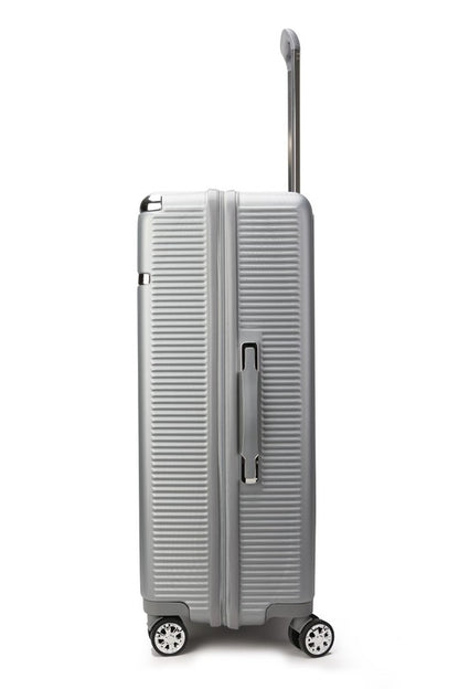 Silver hard-shell suitcase with vertical ribbed texture, extended telescopic handle, and four spinner wheels—positioned upright on a wooden floor.