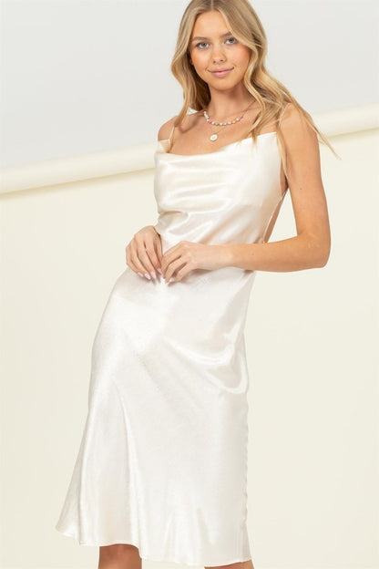 Woman wearing a white satin cowl neck midi dress with spaghetti straps, styled against a light background.