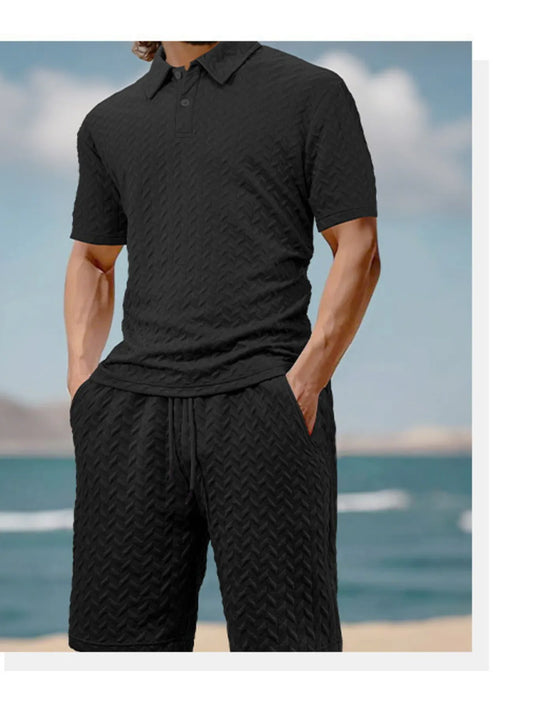 Person wearing a black textured polo shirt and shorts with a blurred beach background