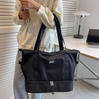 A lady holding a black tote bag with black handles and dual zippered compartments, set against a soft indoor background. Chic and practical—ideal for gym, travel, or daily use.