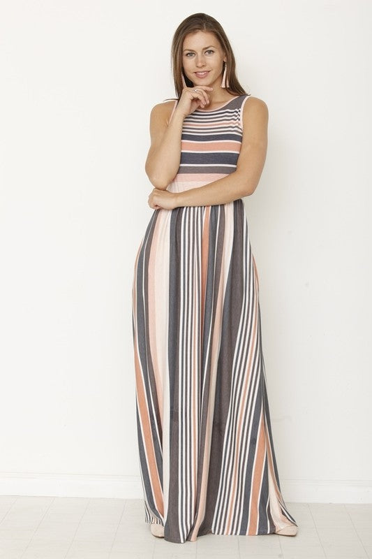 A woman in a long striped dress stands with her back to the camera, looking down slightly. The dress has a mix of gray, peach, and white stripes. She's against a plain white wall with a light-colored floor.