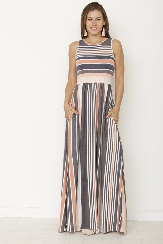 A woman in a long striped dress stands with her back to the camera, looking down slightly. The dress has a mix of gray, peach, and white stripes. She's against a plain white wall with a light-colored floor.