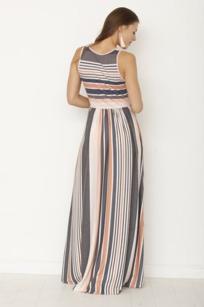 A woman in a long striped dress stands with her back to the camera, looking down slightly. The dress has a mix of gray, peach, and white stripes. She's against a plain white wall with a light-colored floor.