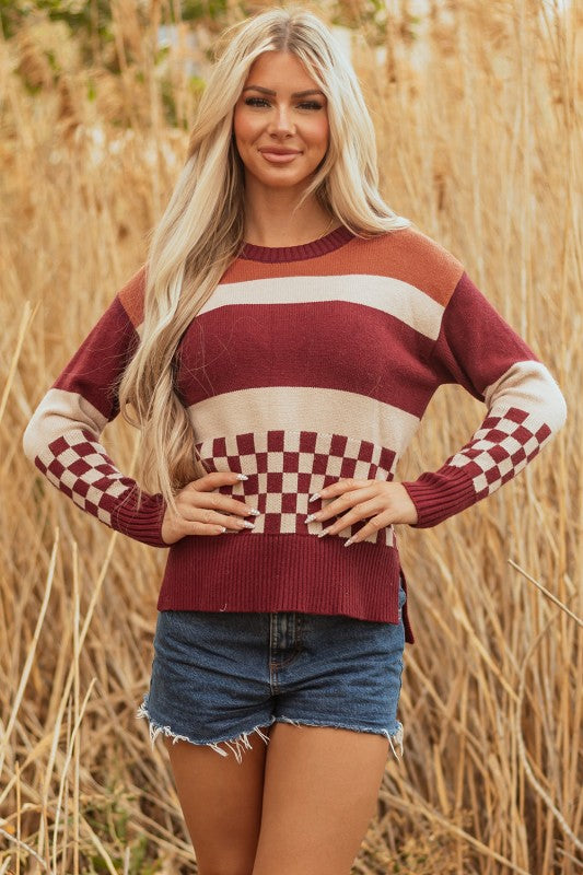 Woman models a checkered color block sweater, featuring a crew neck, perfect for a cozy and stylish look, posing with hands on waist.