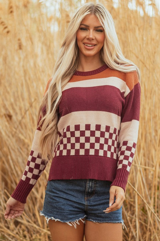 Woman models a checkered color block sweater, featuring a crew neck, perfect for a cozy and stylish look, with hands swerving in motion.