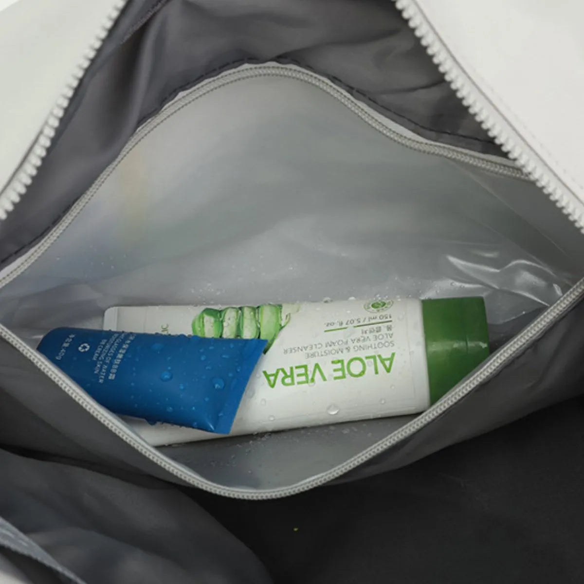 Partially opened travel pouch containing two skincare tubes—one labeled "ALOE VERA" in green and white, and another blue and white tube with water droplets. A clean, organized setup that suggests personal care and travel readiness.