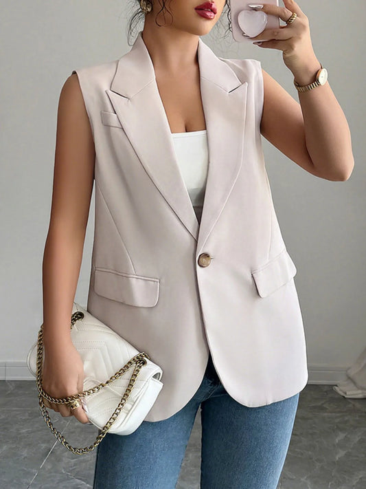 The lady is rocking a sleeveless light pink blazer vest over a white top with blue jeans. She's holding a white purse with a gold chain.