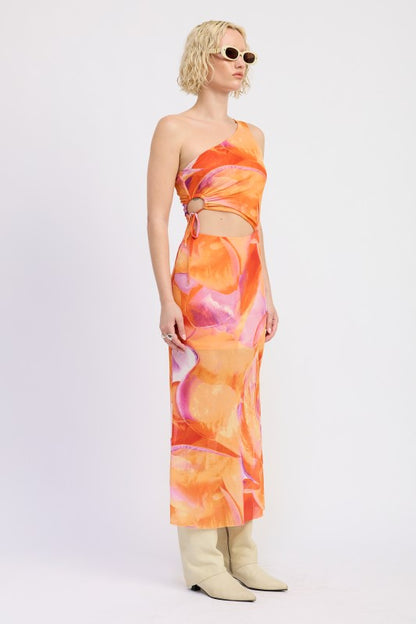 A lady on a one-shoulder maxi dress with an abstract orange, pink, and yellow print. 