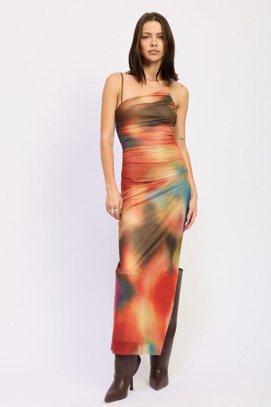 A woman wearing a vibrant, multicolored one-shoulder maxi dress with brown boots, posing against a plain white background.