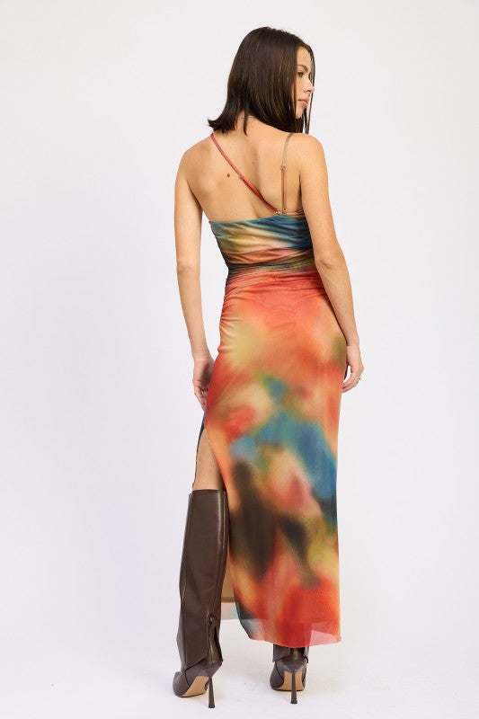 A woman wearing a vibrant, multicolored one-shoulder maxi dress with brown boots, posing against a plain white background.