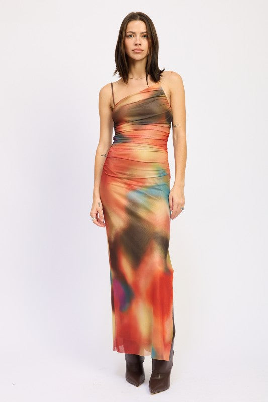 A woman wearing a vibrant, multicolored one-shoulder maxi dress with brown boots, posing against a plain white background.