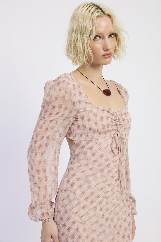 A woman with short blonde hair wearing a pink dress with a pattern and brown boots.