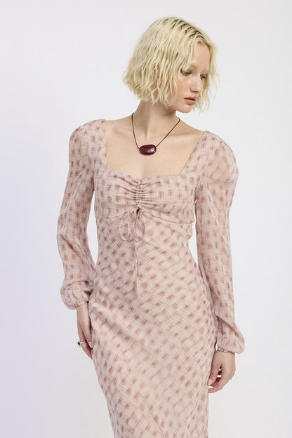 A woman with short blonde hair wearing a pink dress with a pattern and brown boots.