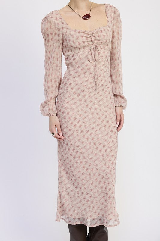 A woman with short blonde hair wearing a pink dress with a pattern and brown boots.