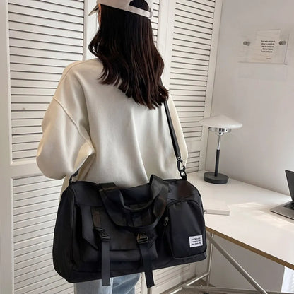 A woman in a white oversized sweatshirt and light-colored cap stands indoors, carrying a large black duffel bag with a “FASHION MINI GIRL” label.