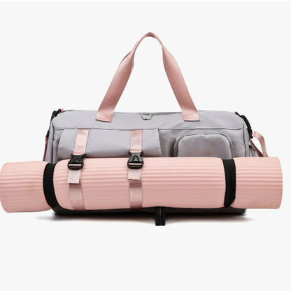 Light gray gym or travel bag with pink handles, featuring a front zip pocket and side compartments. A pink yoga mat is securely attached to the front with black straps—stylish and functional for active lifestyles.