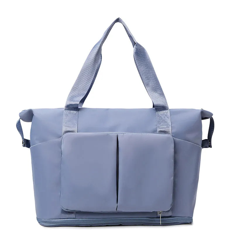 Light blue tote bag with dual shoulder straps, vertical front pockets, side compartments, and a bottom zip section. Made from smooth, water-resistant material—ideal for gym, travel, or everyday use.