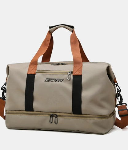 Beige duffel bag with orange handles and black vertical straps, featuring a zippered bottom compartment and front pocket label. Bold and functional—ideal for travel, gym, or everyday use.
