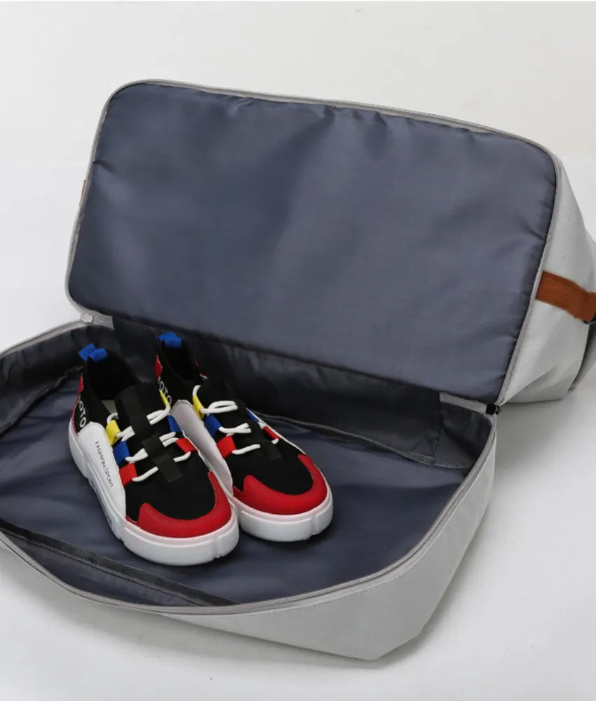 A pair of vibrant sneakers—featuring red, black, white, blue, and yellow accents—are placed inside an open gray travel bag with a brown side strap. The spacious interior and colorful shoes highlight the bag’s practicality and style for organized storage or transport.