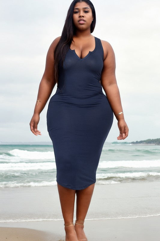 A woman with long dark hair is standing on a beach wearing a navy blue bodycon dress and strappy heels. Waves are crashing in the background under a cloudy sky.