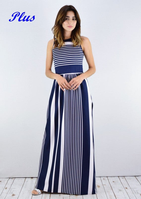 A woman in a blue and white striped maxi dress with a halter neck, posing against a white wall on a wooden floor.
