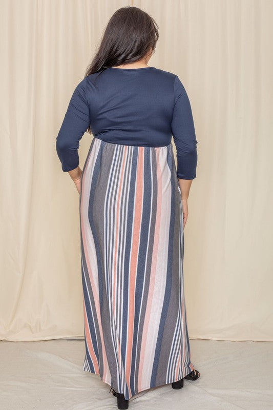 A woman with long dark hair posing in a navy blue top with a striped maxi skirt. The skirt has vertical stripes in shades of blue, pink, white, and gray. 