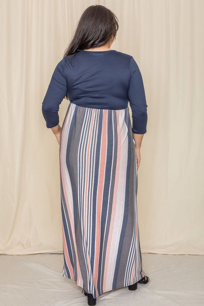 A woman with long dark hair posing in a navy blue top with a striped maxi skirt. The skirt has vertical stripes in shades of blue, pink, white, and gray. 