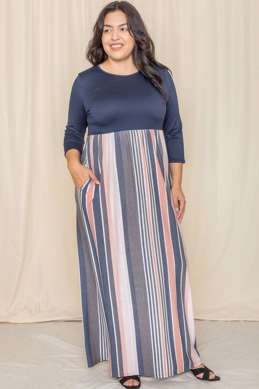 A woman with long dark hair posing in a navy blue top with a striped maxi skirt. The skirt has vertical stripes in shades of blue, pink, white, and gray. 