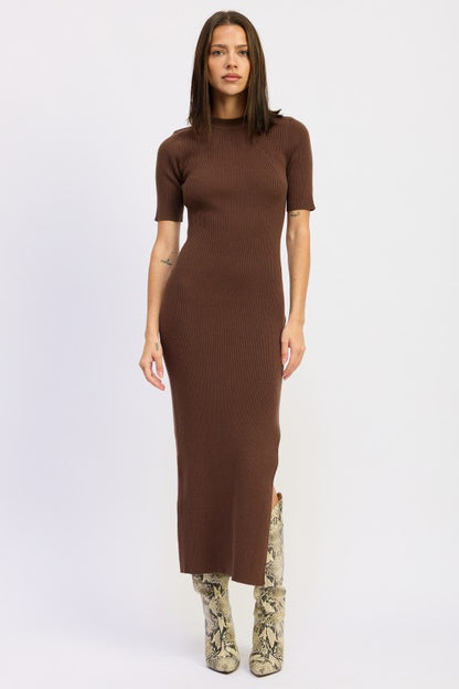 Woman wearing a ribbed knit sweater dress with side slit, styled with knee-high boots and minimalist accessories.