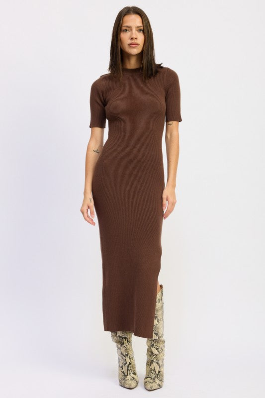 Woman wearing a ribbed knit sweater dress with side slit, styled with knee-high boots and minimalist accessories.