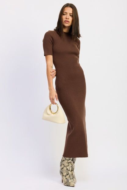 Woman wearing a ribbed knit sweater dress with side slit, styled with knee-high boots and minimalist accessories.